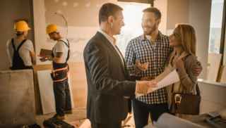 Couple speaking to a builder while two tradesmen work on the house